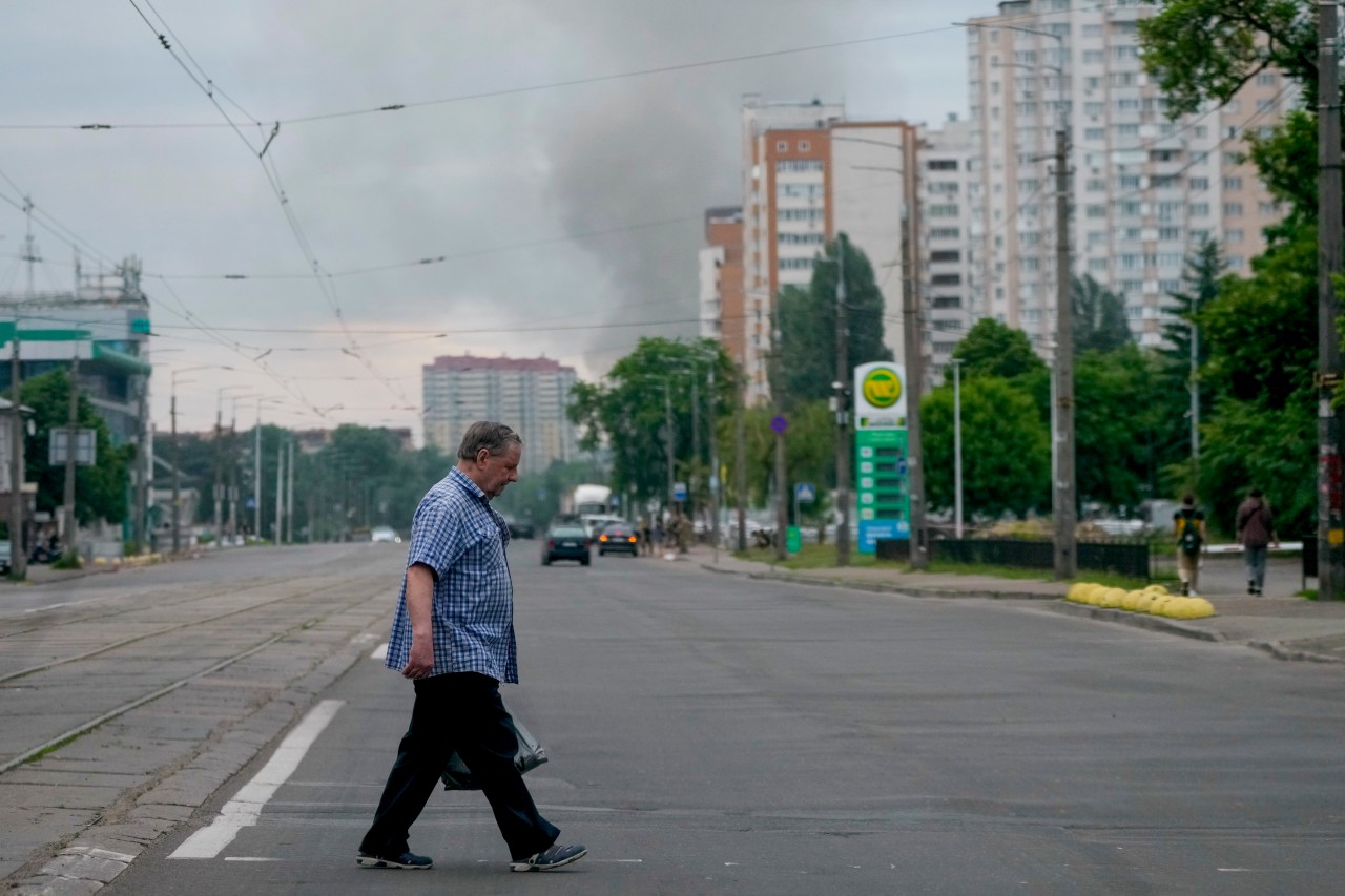 05.06.2022, Ukraine, Kiew: Ein Mann überquert eine Straße, während im Hintergrund schwarzer Rauch aufsteigt. Russland hat nach Angaben des ukrainischen Generalstabs die Hauptstadt und einen Vorort erneut mit Raketen beschossen. 