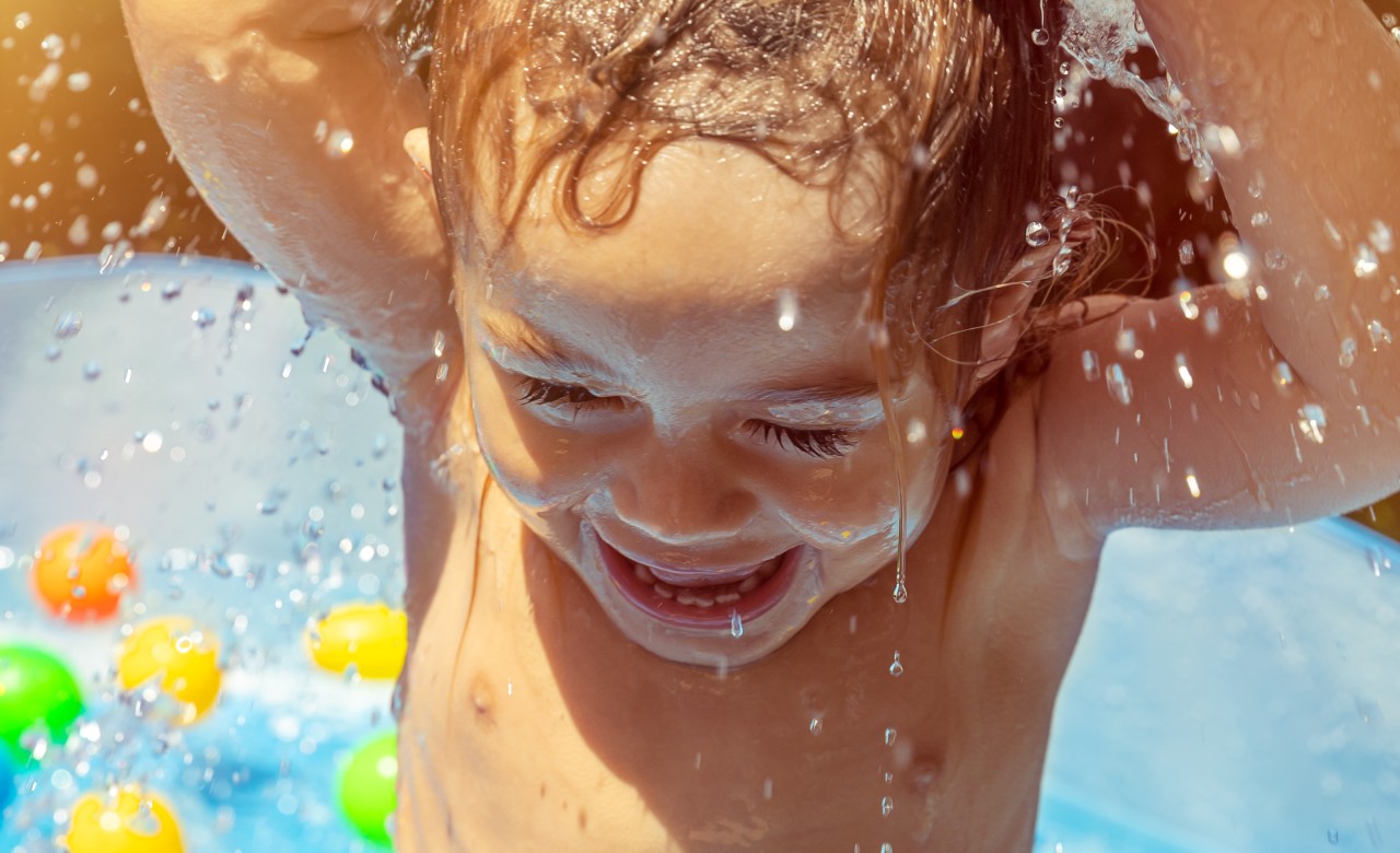 Ein Kind wird wegen der Hitze mit einem Wasserschlauch abgebraust. Danach schreit es vor Schmerzen. (Symbolbild)