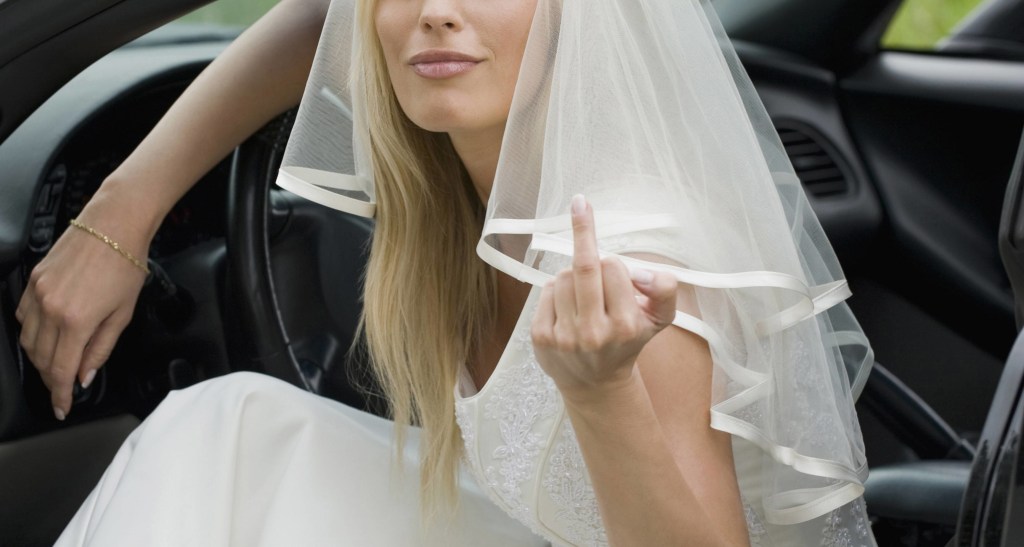 Eine Braut sitzt während ihrer Hochzeit in einem Auto und zeigt den Mittelfinger.