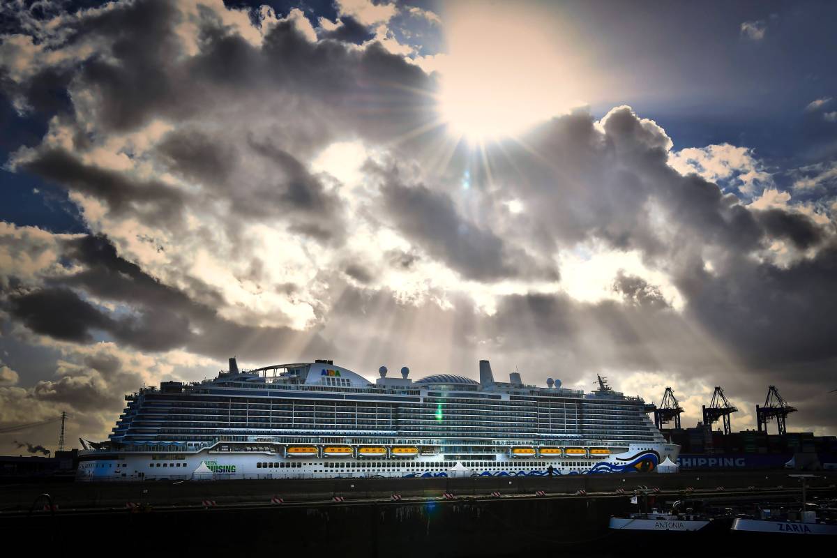 Ein Kreuzfahrt-Schiff der Aida. Über ihm türmen sich Wolken, durch die die Sonne bricht.
