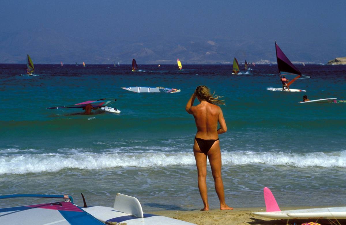 Während ihres Urlaubs in Griechenland beobachtet eine Frau vom Strand aus Windsurfer im Wasser.