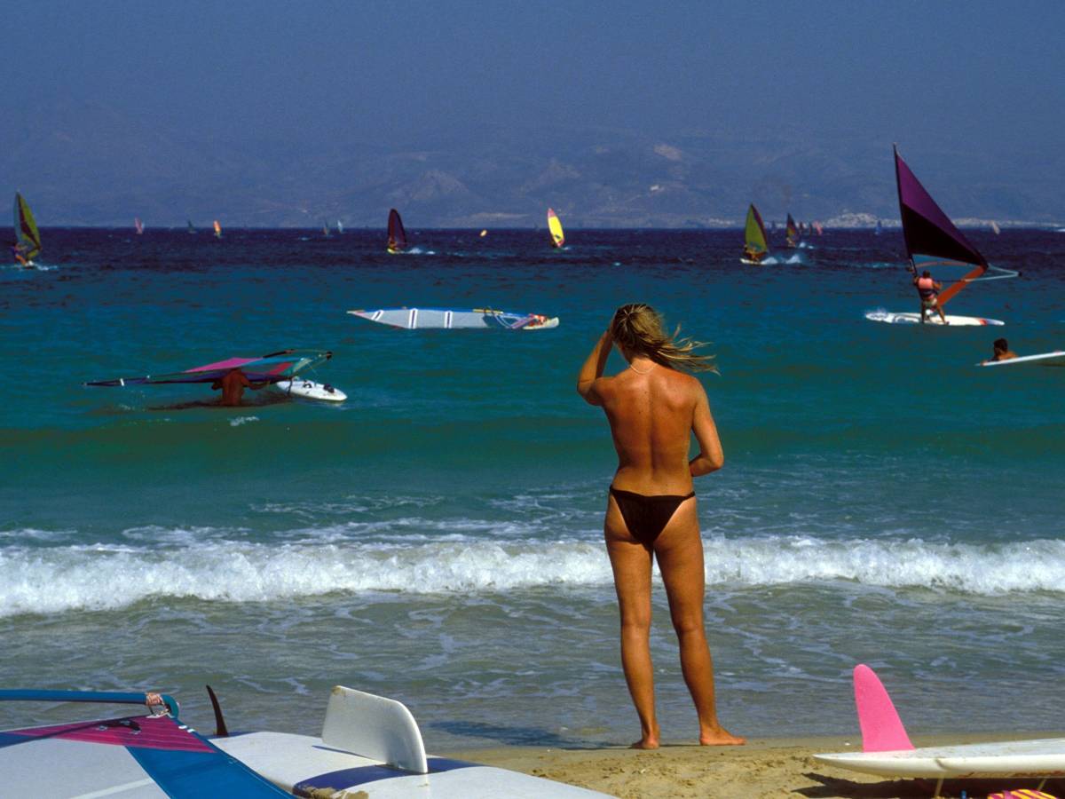 Während ihres Urlaubs in Griechenland beobachtet eine Frau vom Strand aus Windsurfer im Wasser.