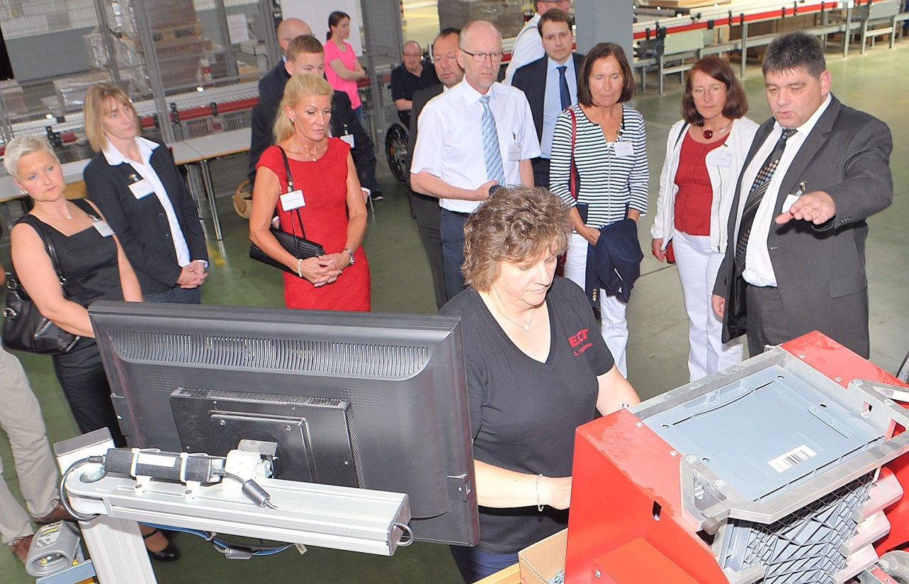 Ein Gruppen besuchen die Ehrengäste der Eröffnung das neue Logistikzentrum und schauen den Mitarbeitern über die Schulter.
