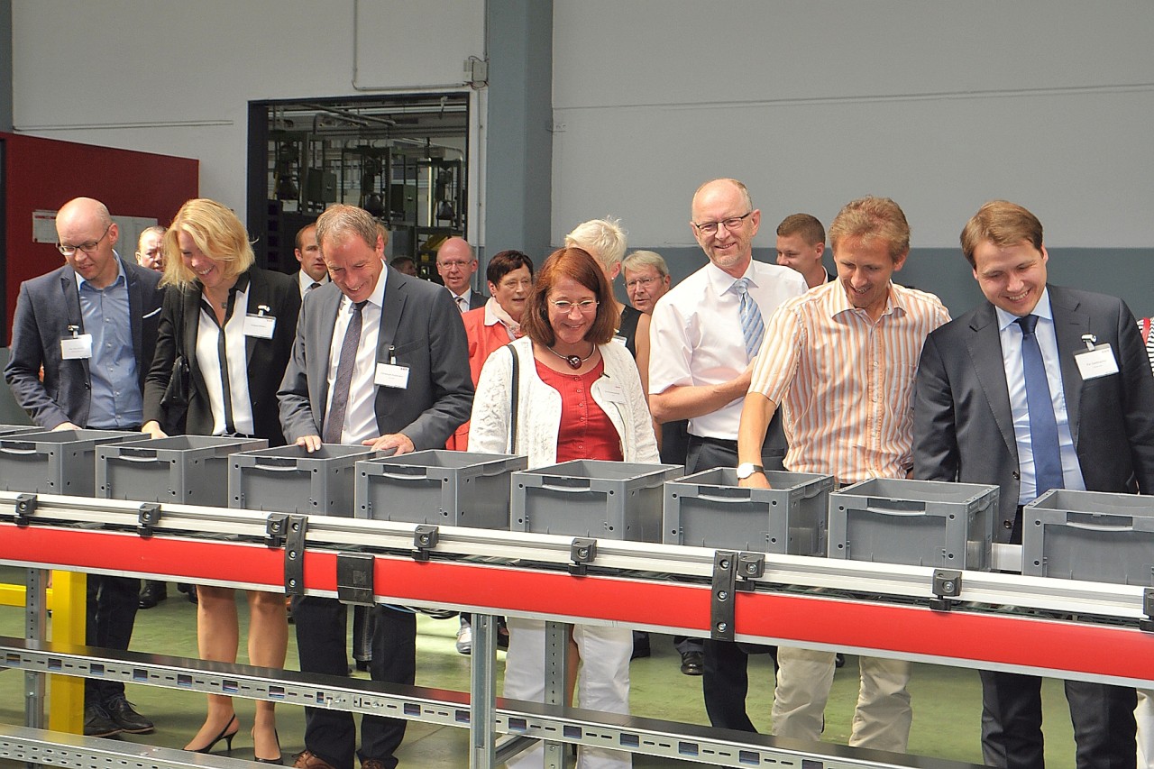 Ein Gruppen besuchen die Ehrengäste der Eröffnung das neue Logistikzentrum und schauen den Mitarbeitern über die Schulter.