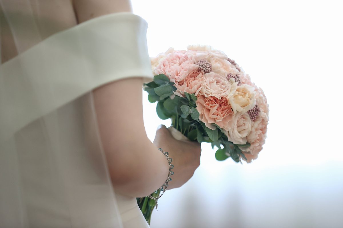 Frau im Hochzeitskleid von hinten mit Blumenstrauß