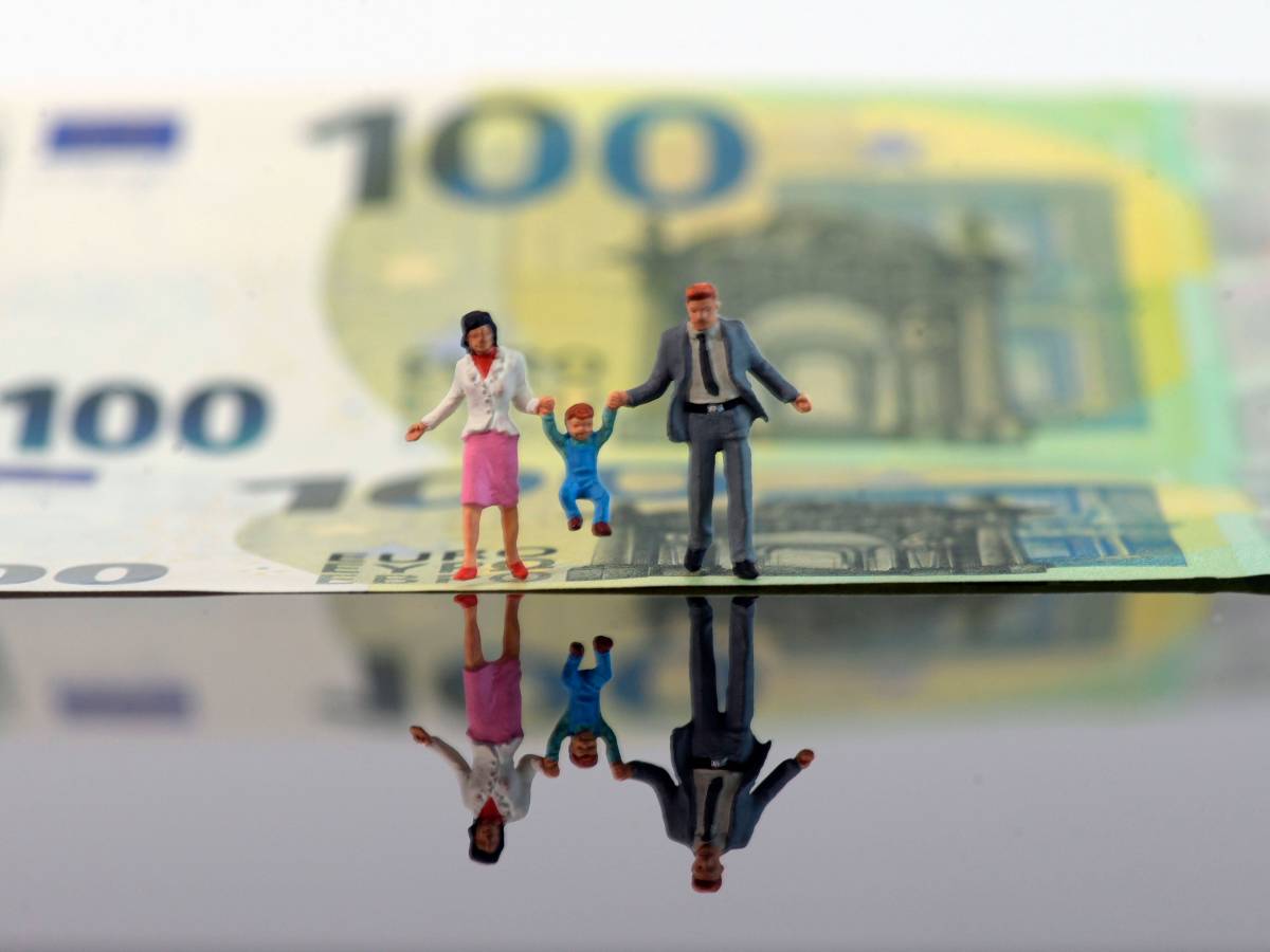 Figuren von zwei Erwachsenen halten ein Kind an ihren Händen. Im Hintergrund ein 100-Euro-Schein.