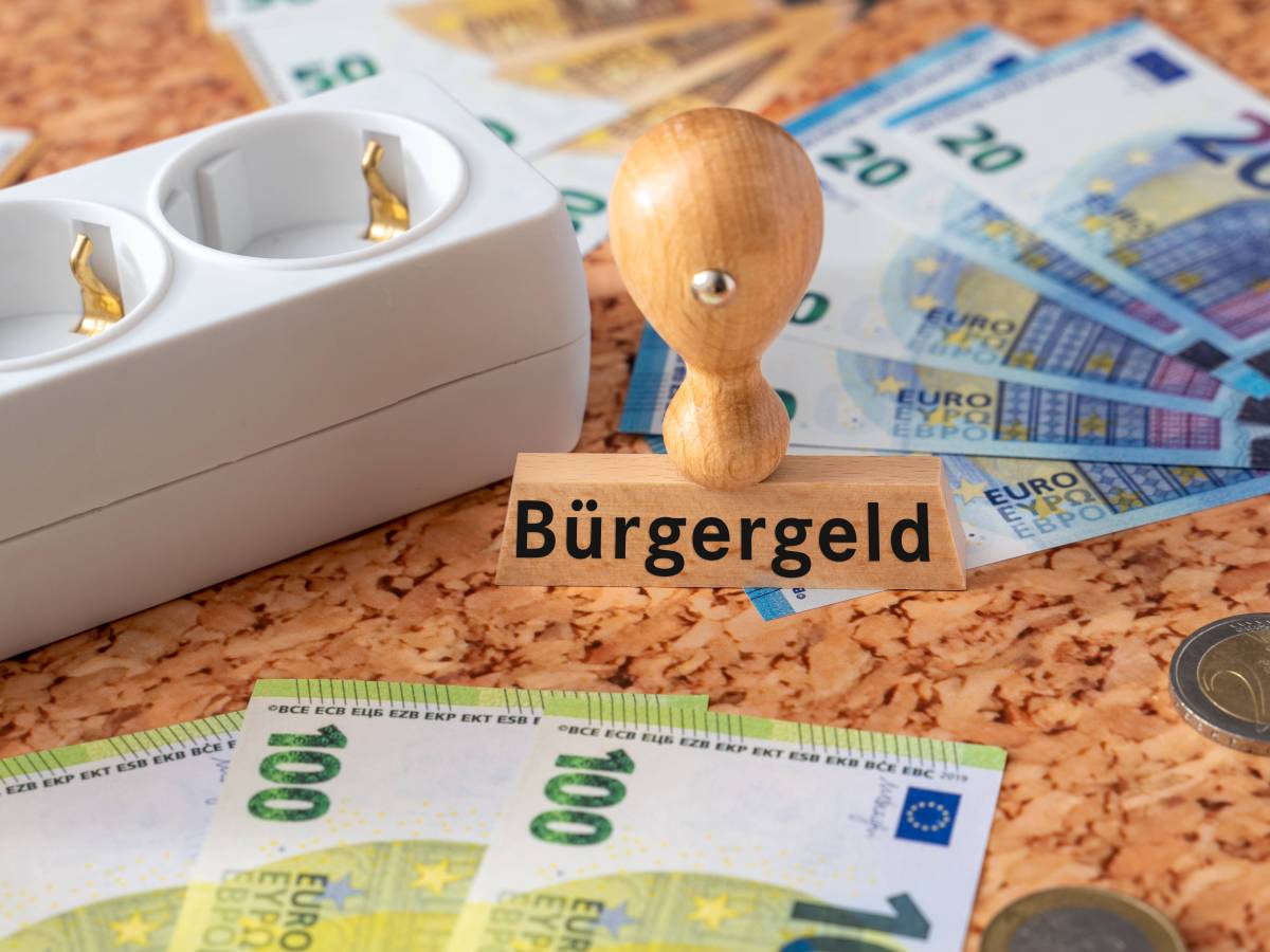 Ein Stempel mit dem Aufdruck Bürgergeld sowie viele Euro-Geldscheine und eine Steckdosenleiste.