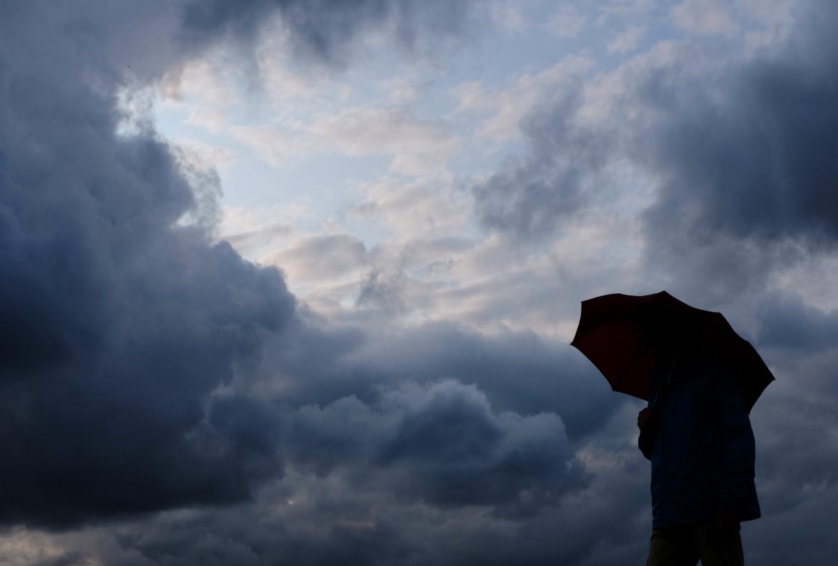 Person mit Regenschirm schaut in Gewitterhimmel