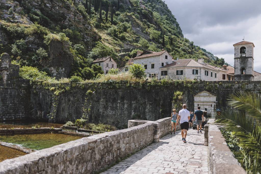 Passanten gehen über eine gepflasterte Brücke in der historischen Altstadt von Kotor.