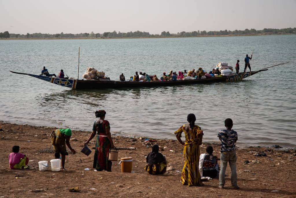 Menschen stehen am Ufer eines Sees, auf dem ein Boot ablegt.