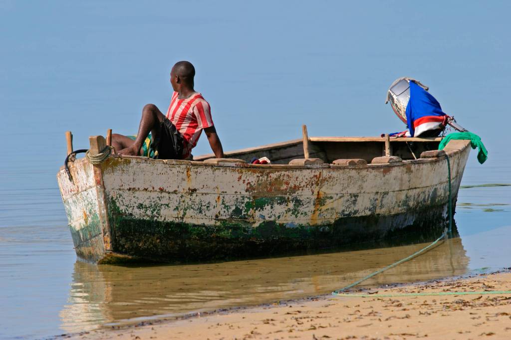 Ein Fischer sitzt auf einem Holzboot am Ufer eines Sees.