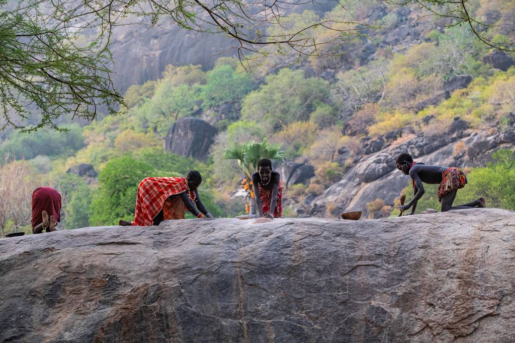 Junge Mädchen mahlen Sorghum auf einem Felsen, Stamm der Laarim, Boya Hills, Ost-Äquatoria, Südsudan,