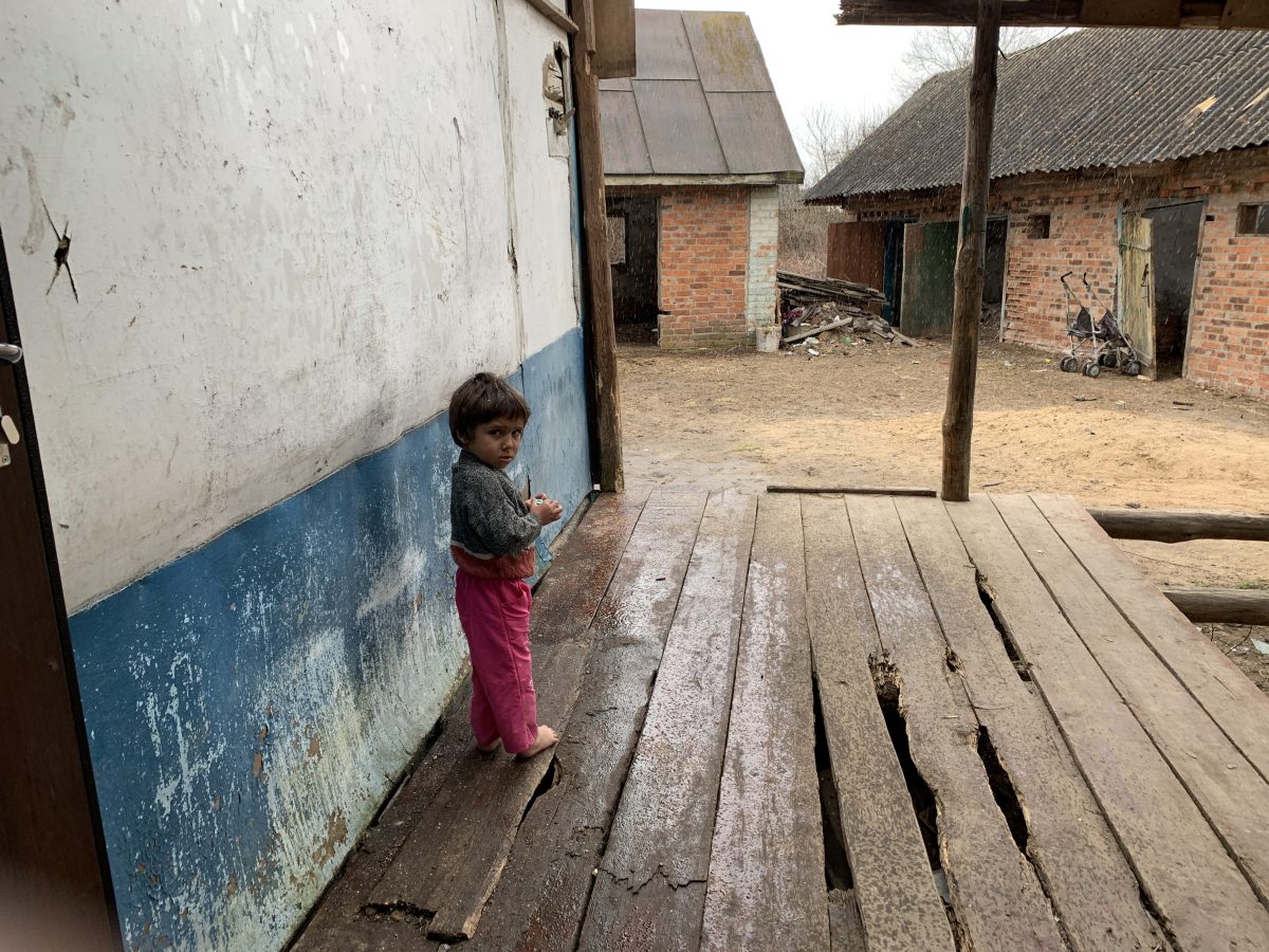 Ein Kleinkind steht vor einem Haus in einer Armutsgegend in der Ukraine.