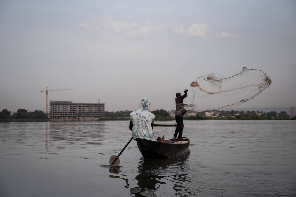 Ein Mann wirft ein Fischernetz von einem Boot aus ins Wasser eines Sees.