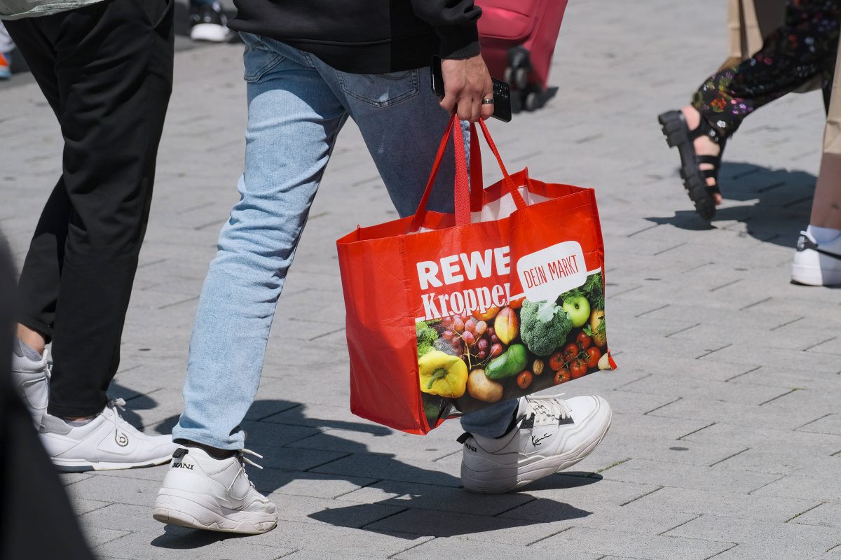 Frau trägt Rewe-Tragetasche