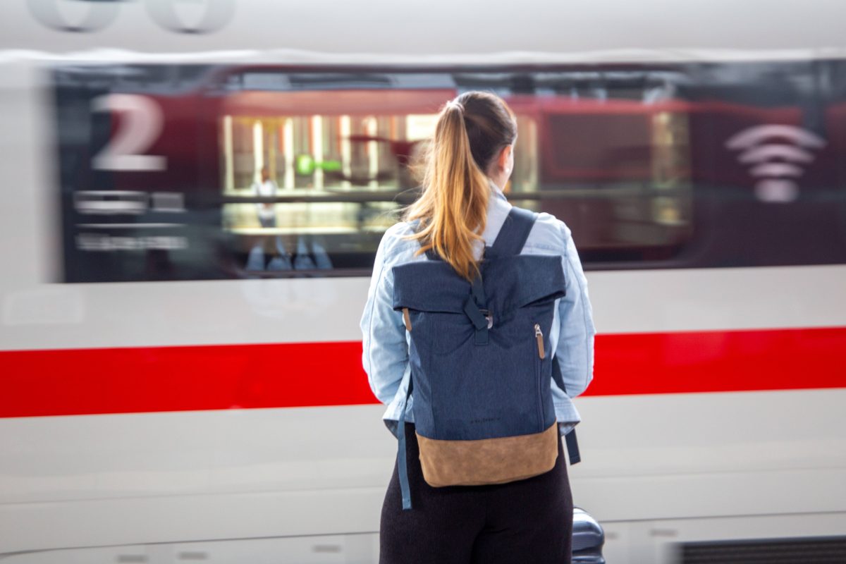 Frau seht vor einem vorbeifahrenden Zug der Deutschen Bahn