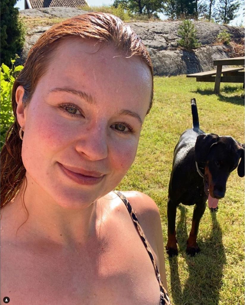 Alexandra Andresen steht in einem Garten und macht ein Selfie mit einem Hund im Hintergrund.