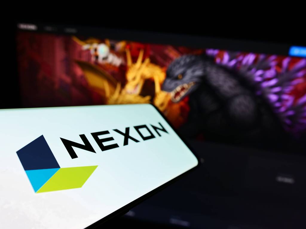 Ein Smartphone mit dem Firmenlogo von Nexon ist vor einem Computer-Monitor zu sehen, auf ein ein Online-Game gespielt wird.