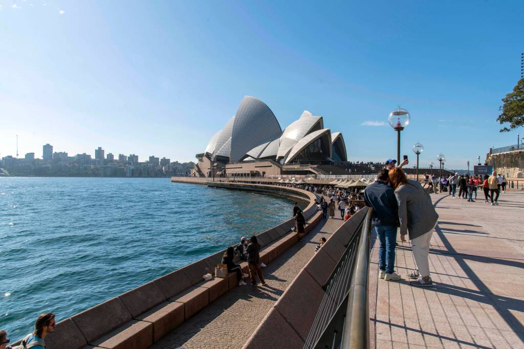 Passanten stehen vor dem im Hintergrund zu sehenden Sydney Opera House, das direkt am Pazifik liegt.