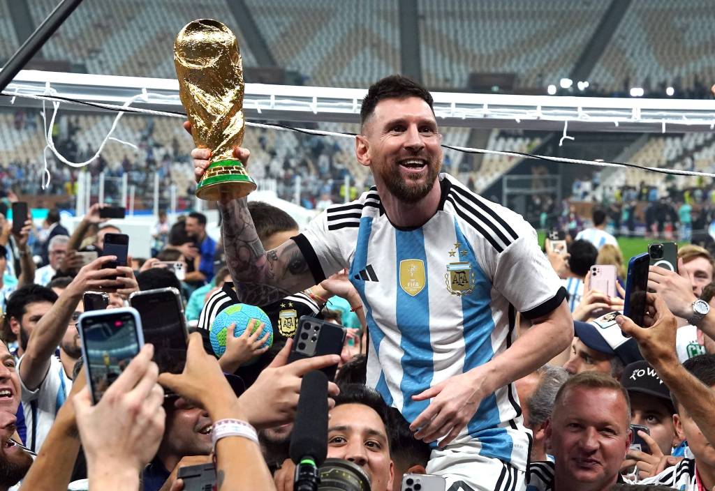 Lionel Messi hält den WM-Pokal inmitten einer Menschentraube.