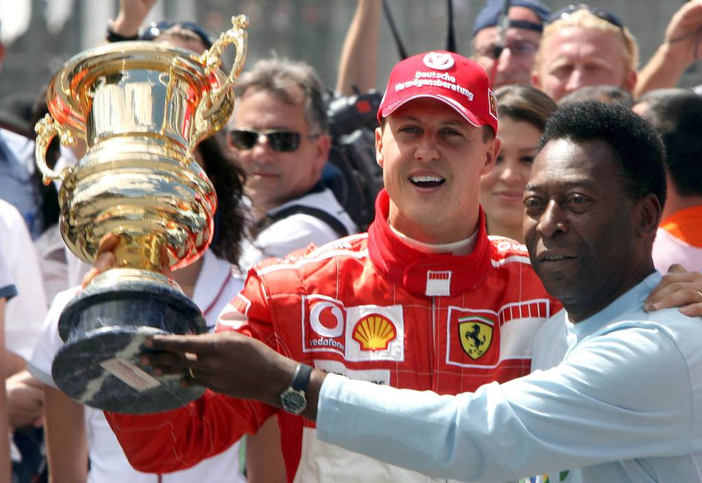 Michael Schumacher posiert mit der einstigen Fußball-Legende Pelé mit einem goldenen Pokal vor Fans.