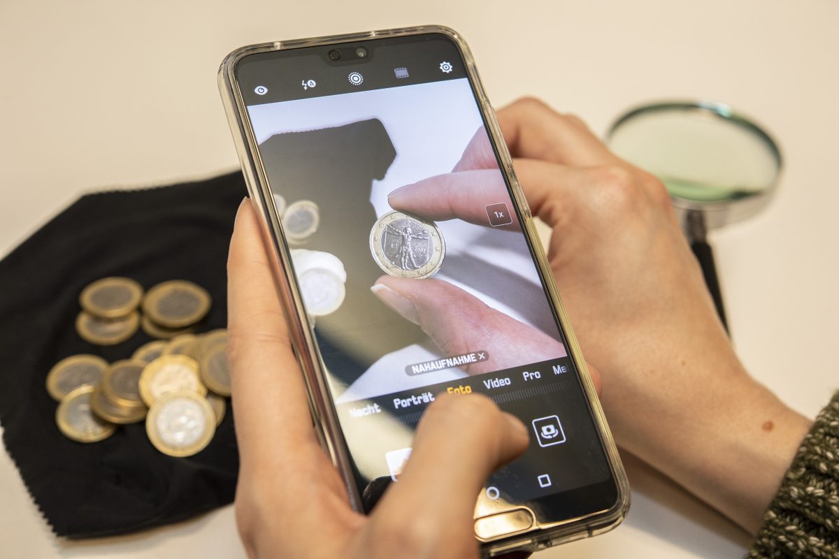 Eine Frau schaut sich auf einem Handy Euro-Münzen an.