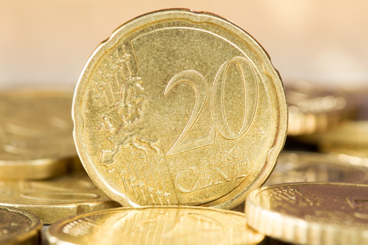 Eine 20-Cent-Euromünze steht senkrecht und mit der Vorderseite nach vorn zwischen weiteren liegenden Cent-Münzen.