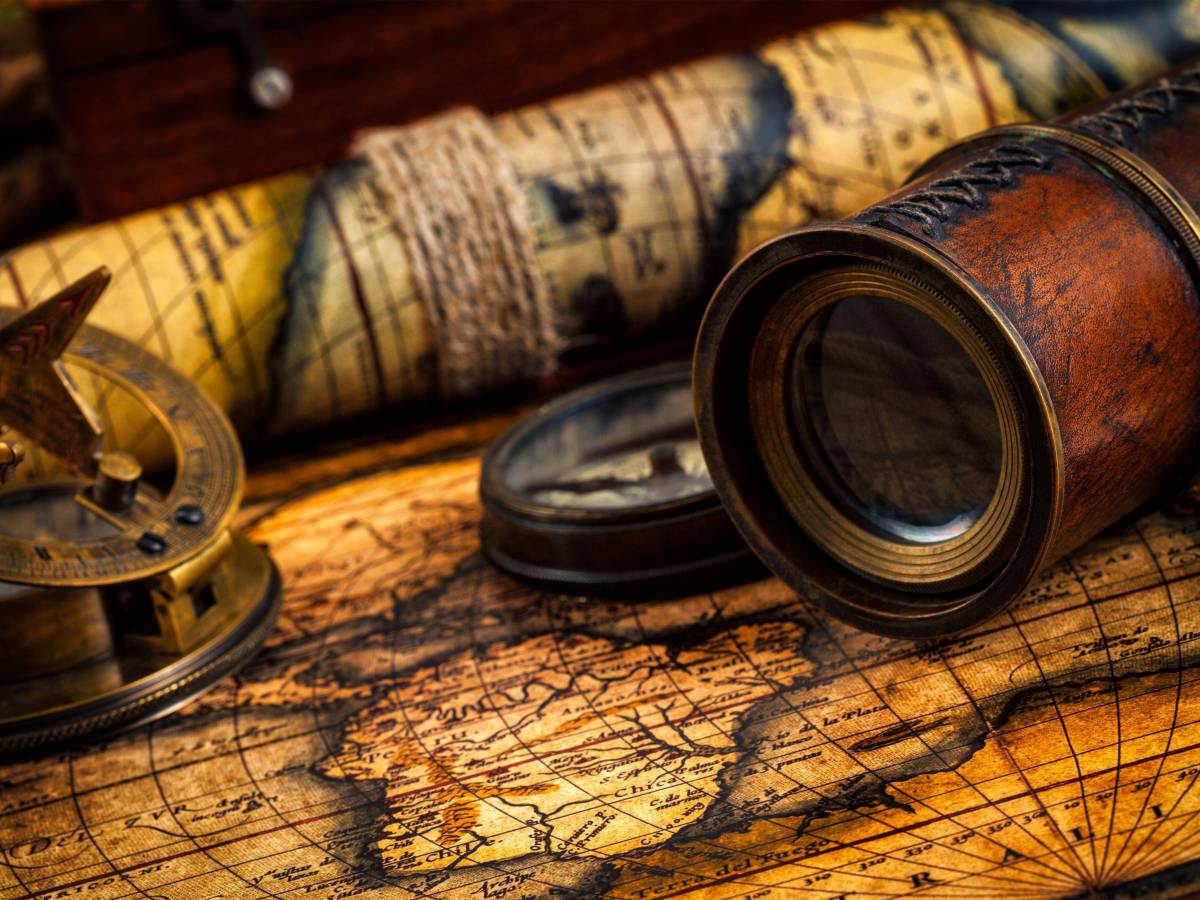 Ein alter Kompass liegt mit einer Messing-Sonnenuhr, einem mit Leder vermantelten Fernrohr auf einer vergilbten, alten Weltkarte.
