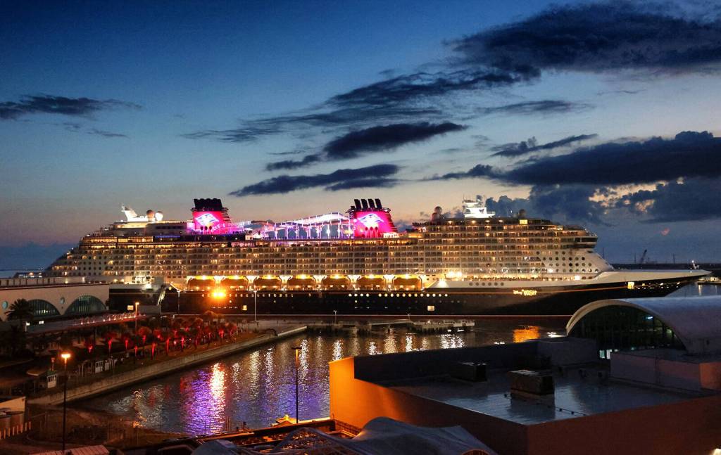 Ein beleuchtetes Kreuzfahrtschiff bei Nacht am Hafen.