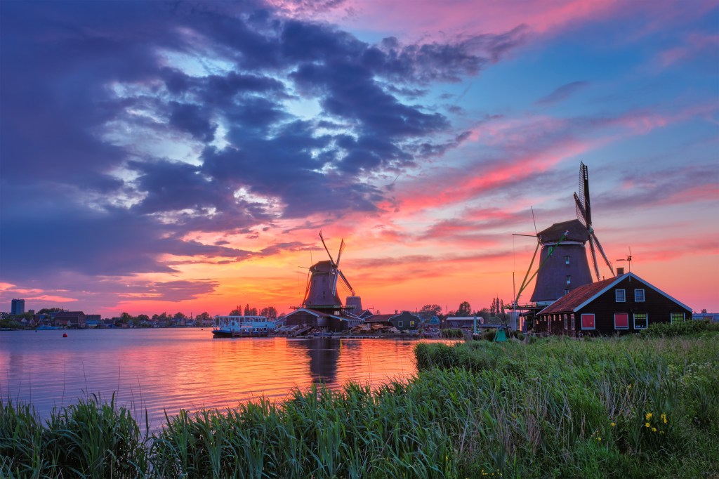 Windmühlen am Flussufer in den Niederlanden bei Sonnenuntergang mit dramatischem Himmel.