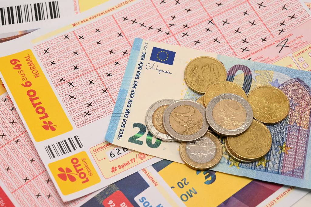 Auf einem Lottoschein liegt ein 20-Euro-Scheim und Münzgeld.