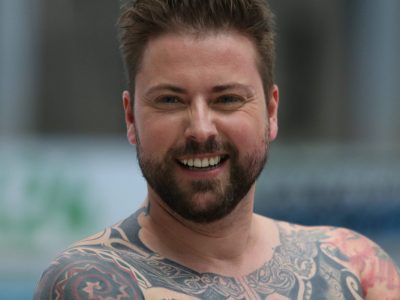 Schauspieler Felix von Jascheroff in einer horizontalen Portraitaufnahme. Er lächelt, hat braune hochgegelte Haare. Man sieht ebenfalls Tattoos auf seinem Oberkörper.