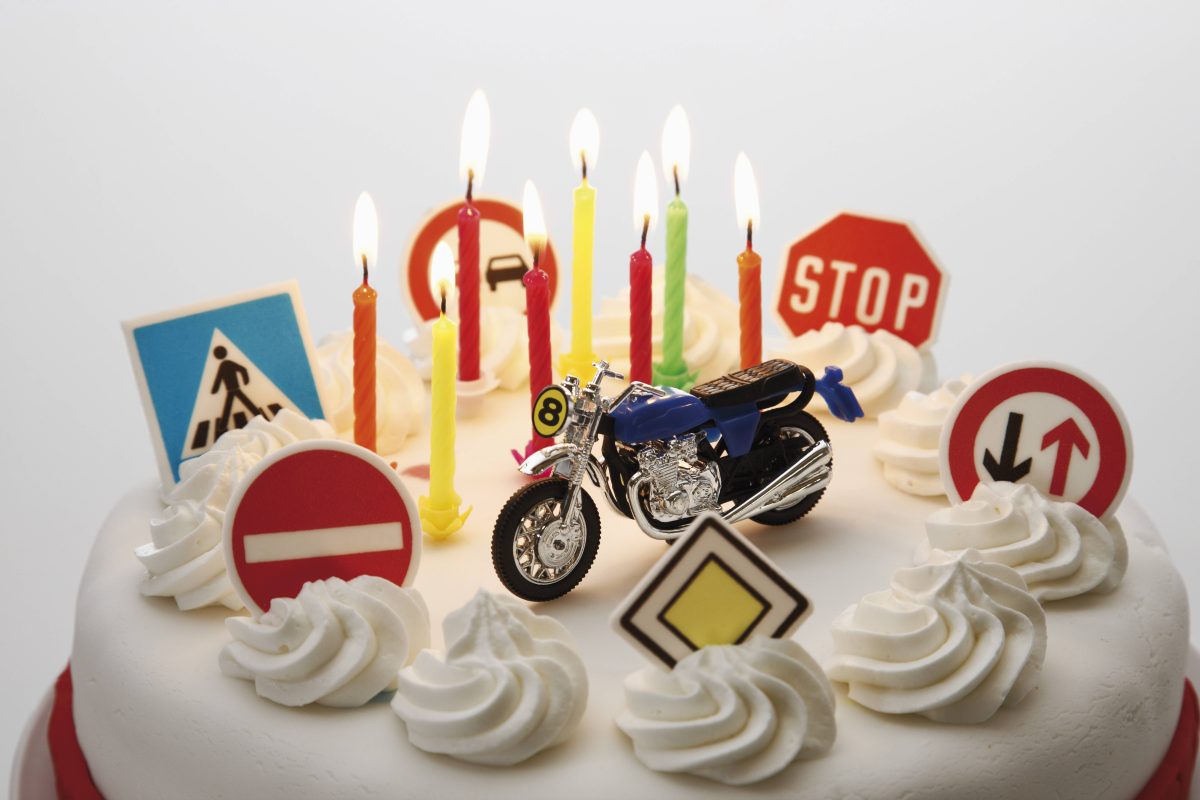 Auf dem Bild sieht man einen Kuchen in weiß. Oben auf dem Kuchen sind fünf Sahnehäufchen und acht Kerzen. In der Mitte des Kuschens steht ein blaues Motorrad und drum herum stehen verschiedene Verkehrsschilder.