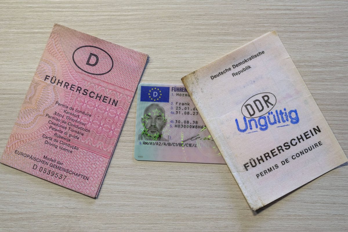 Auf einem Holztisch liegen drei verschiedene Führerscheine. Links liegt ein alter Papier-Führerschein, in der Mitte ein Kartenfrüherschein und ganz Rechts ein Führerschein aus der DDR. Auf dem Führerschein Rechts steht außerdem in blau "Ungültig"