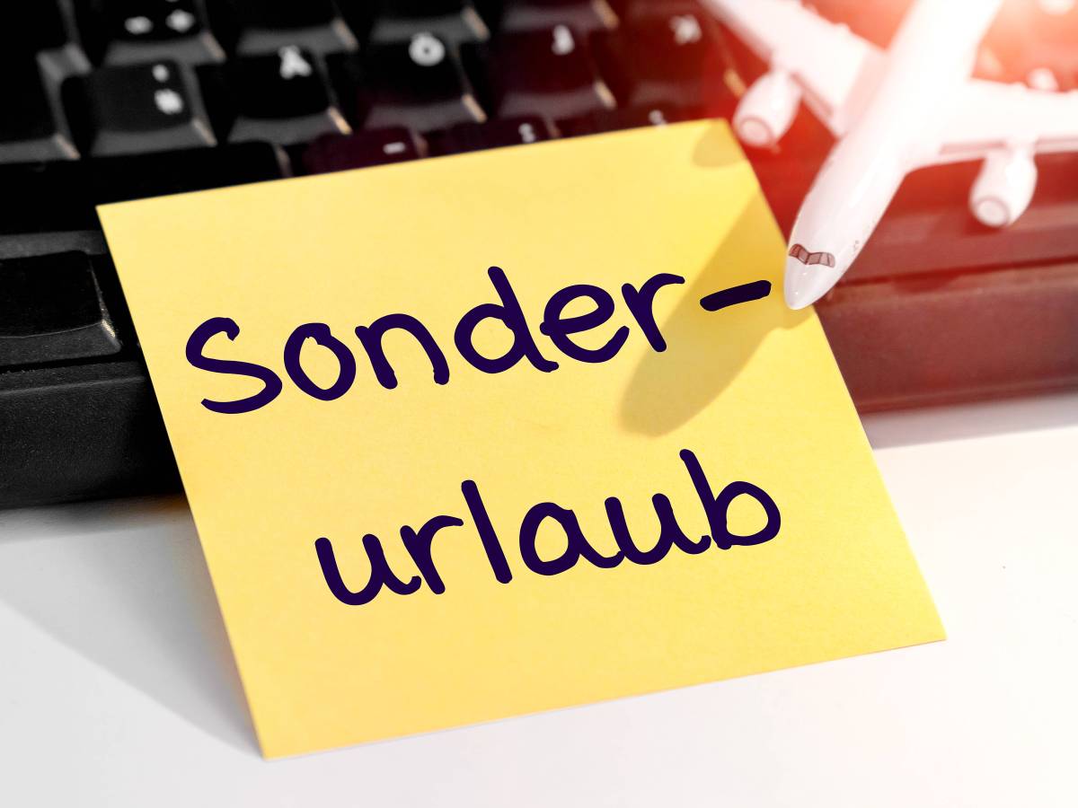 Auf einer schwarzen Tastatur ist ein gelber Zettel angelehnt. Auf dem Zettel steht mit schwarzer Schrift "Sonderurlaub". Oben Rechts im Bild ist außerdem ein weißes Flugzeug.