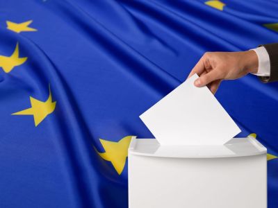 Eine Hand legt einen EU-Wahlzettel in die Wahlurne
