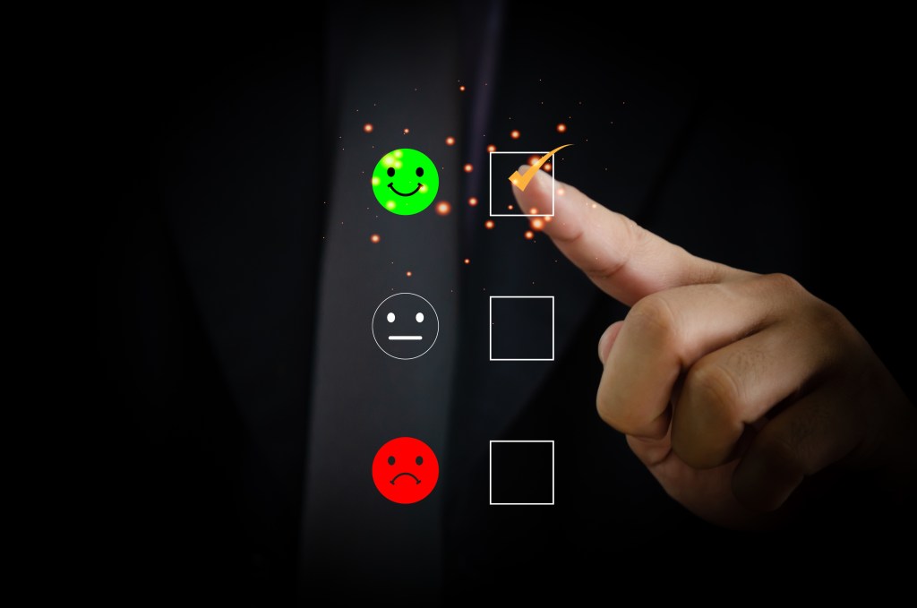 Ein Finger wählt zwischen einem grinsenden, einem neutralen und einem traurigen Smiley, den fröhlichen.