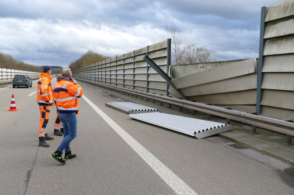 Auf der Autobahn A560 bei Hennef: stehen Arbeiter vor den Teilen einer Lärmschutzwand, die der Sturm beschädigt hat.